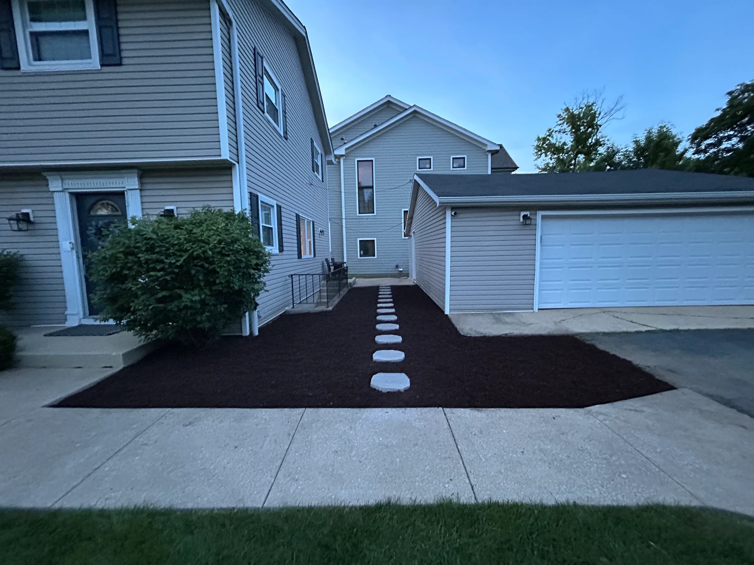 Stepping-stone route through a mulched bed between a house and garage