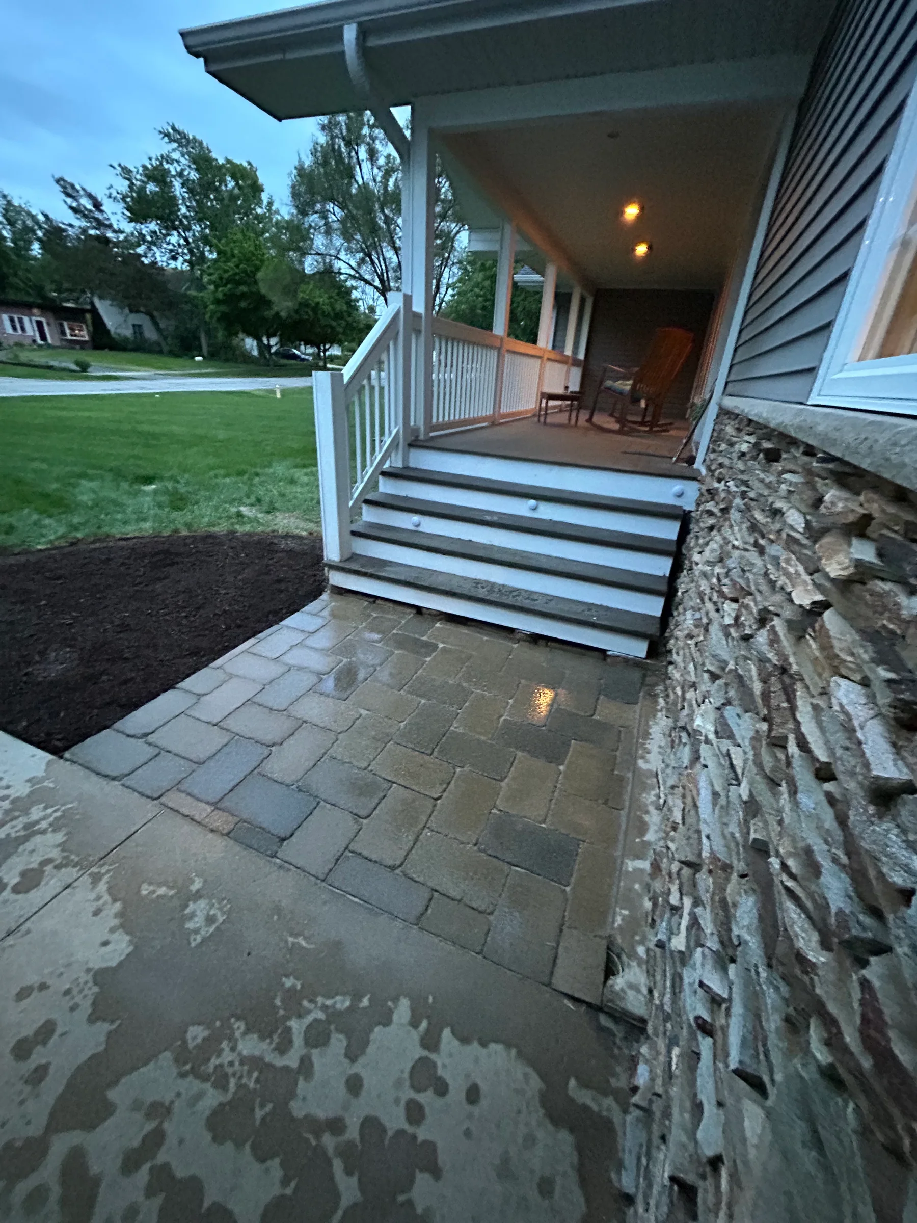 Paver entry walk beside a stone-clad house and porch steps