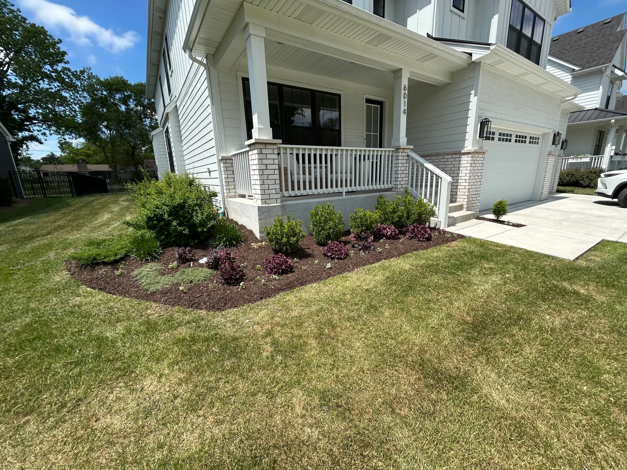 Fresh mulch and shrubs around a white front porch